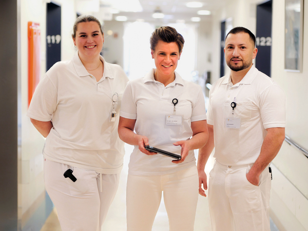 Physician Assistant Hanna Lübbe, Zentrumsleiterin Dr. med. Julia M. Reinke mit Tablet-Computer in der Hand und Facharzt Irakli Paatishvili stehen nebeneinander in weißer Funktionskleidung im Stationsflur und blicken in die Kamera im auf Hüftprothesen, Knieprothesen und Schulterprothesen spezialisierten Albertinen Endoprothetikzentrum Hamburg Physician Assistant Hanna Lübbe, Zentrumsleiterin Dr. med. Julia M. Reinke mit Tablet-Computer in der Hand und Facharzt Irakli Paatishvili stehen nebeneinander in weißer Funktionskleidung im Stationsflur und blicken in die Kamera im auf Hüftprothesen, Knieprothesen und Schulterprothesen spezialisierten Albertinen Endoprothetikzentrum Hamburg