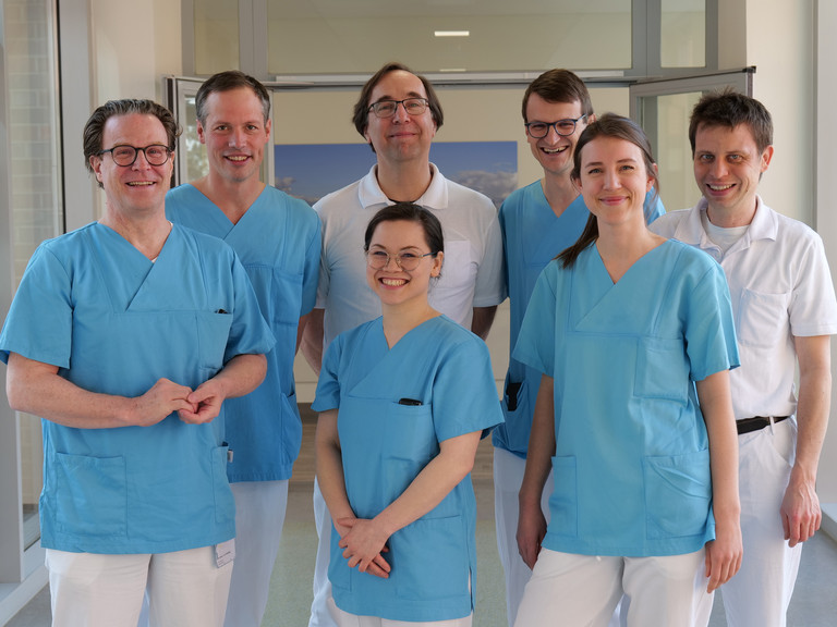 Das Team Des Mitralklappen-Zentrums des Albertinen Herz- und Gefäßzentrums am Standort Hamburg Schnelsen lächelt auf einem Flur in Arztkleidung in die Kamera Das Team Des Mitralklappen-Zentrums des Albertinen Herz- und Gefäßzentrums am Standort Hamburg Schnelsen lächelt auf einem Flur in Arztkleidung in die Kamera