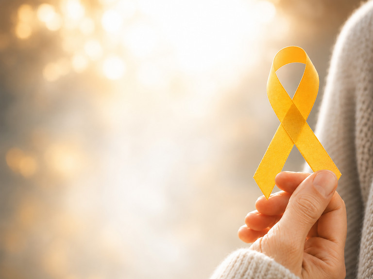 Hand hält eine gelbe Awareness-Schleife als Symbol für Suizidprävention vor einem warmen, hellen Hintergrund. Hand hält eine gelbe Awareness-Schleife als Symbol für Suizidprävention vor einem warmen, hellen Hintergrund.