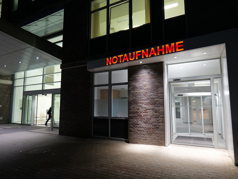 Beleuchteter Eingang der Zentralen Notaufnahme am Albertinen Krankenhaus mit rotem Schriftzug „NOTAUFNAHME“ über den Glastüren. Beleuchteter Eingang der Zentralen Notaufnahme am Albertinen Krankenhaus mit rotem Schriftzug „NOTAUFNAHME“ über den Glastüren.