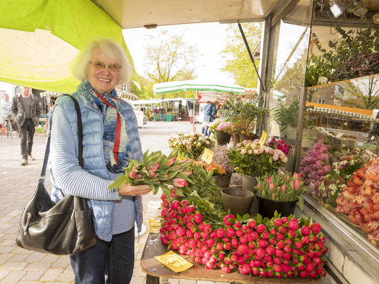 Eine Seniorin kauft auf dem Wochenmarkt Blumen, Beschäftigung in der Residenz am Wiesenkamp, Freizeitangebot in der Seniorenresidenz in Hamburg-Volksdorf